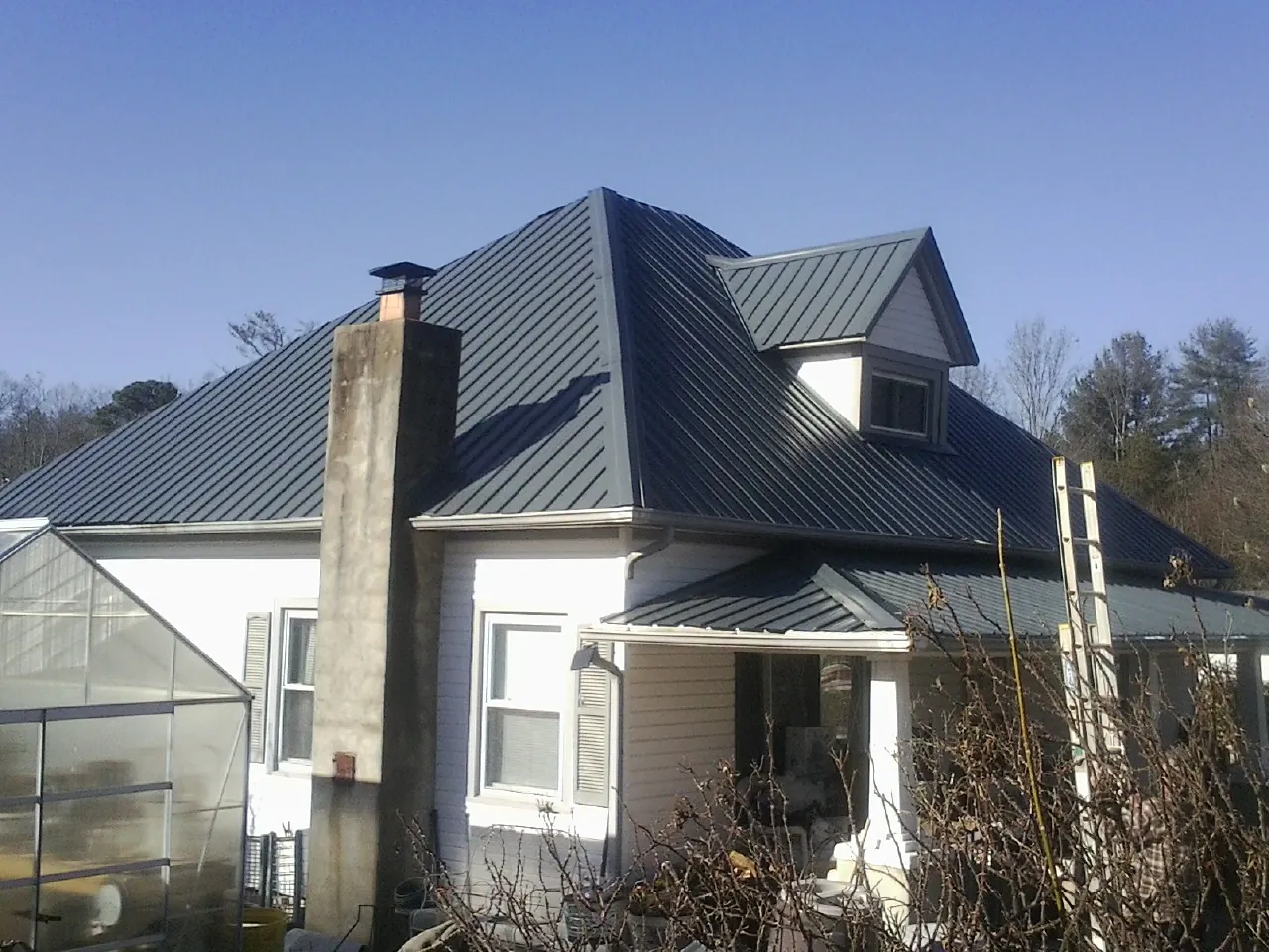 Dark blue standing seam metal roof on a white farmhouse with dormer — Slate & Tile Roof Repair by Roofing Brothers in Beasley