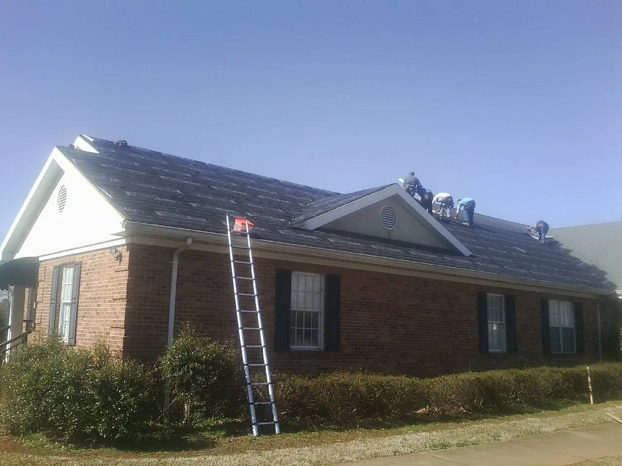 Crew tearing shingles off a brick ranch roof with a ladder set — Emergency Roof Repair work by our crew in Beasley
