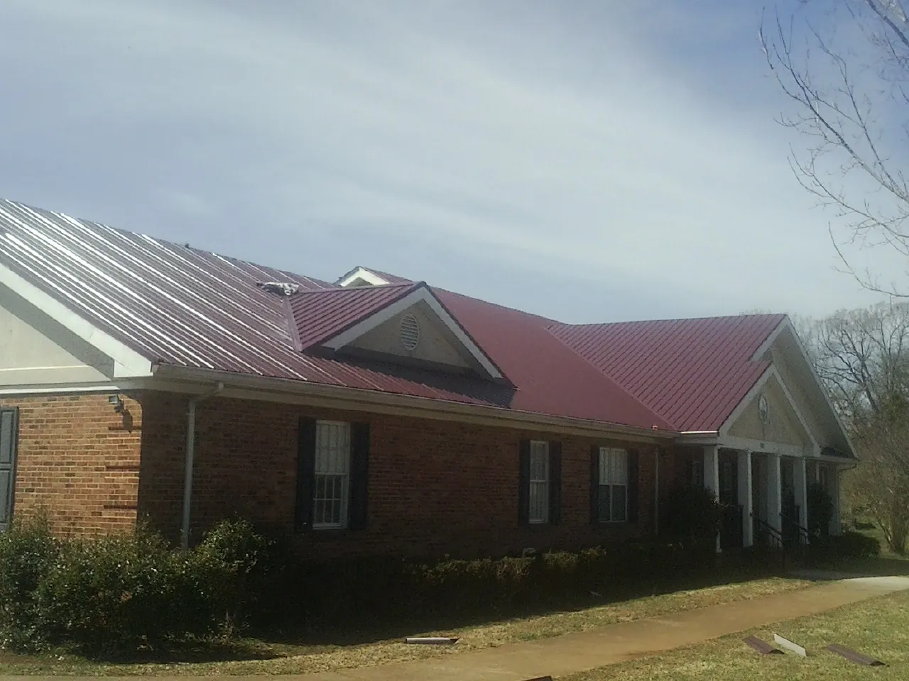 Red metal roof with gabled entries on a long brick building, from a Hail Damage Roof Repair job in Beasley