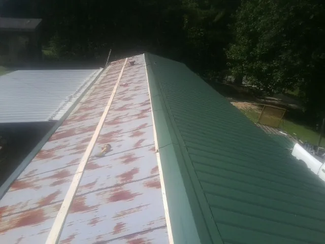 Old rusted panels beside newly installed green metal roofing — Wind Damage Roof Repair by Roofing Brothers in Beasley