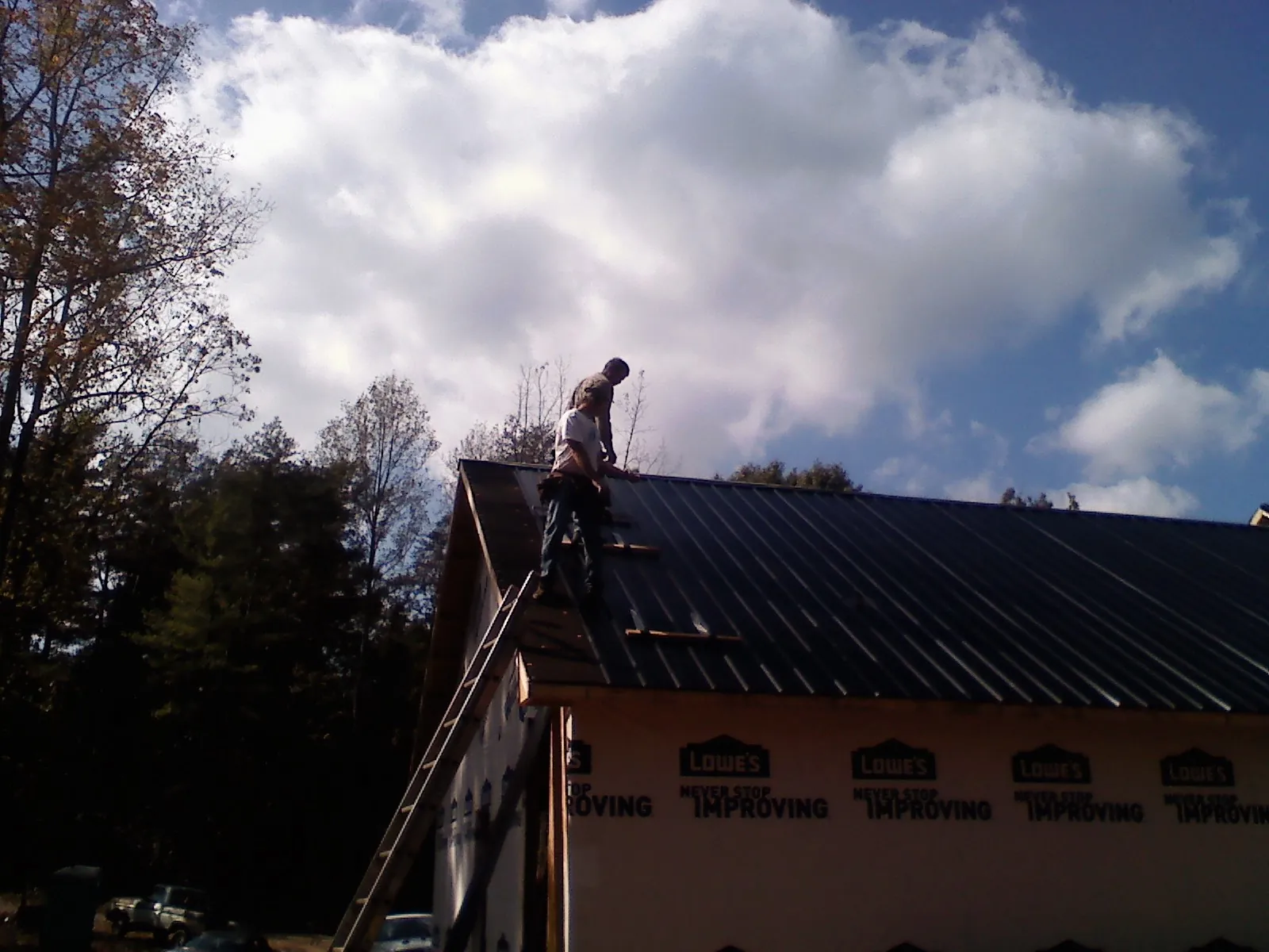 Roofer fastening dark metal panels high against a cloudy sky, from a Roof Inspection job in Beasley